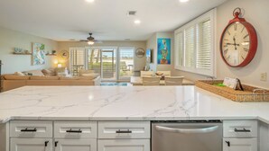A spacious kitchen with a large marble island, white cabinetry, and a red wall clock. - Seascape Boardwalk Villa 199*5 minute walk to beach! (Miramar Beach)