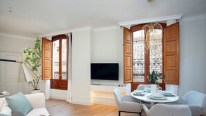 A modern living room with a flat-screen TV, a dining area with a round table and chairs, wooden shutters, and a potted plant. - Genteel Home Bib rambla IV (Granada)