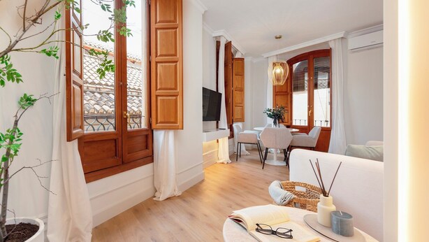 A modern living room with wooden shutters, a dining area with a table and chairs, and a cozy seating area with a sofa and a small side table. - Genteel Home Bib rambla IV (Granada)