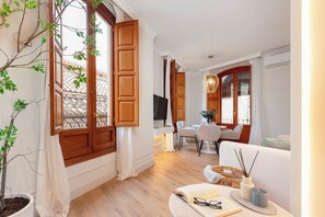 A modern living room with wooden shutters, a dining area with a table and chairs, and a cozy seating area with a sofa and a small side table. - Genteel Home Bib rambla IV (Granada)