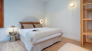A bedroom with a bed, bedside lamp, and a wooden shelf unit. - Genteel Home Bib rambla IV (Granada)