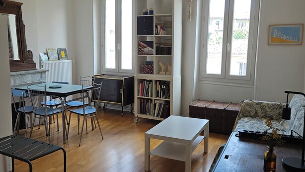 A spacious living room with a wooden floor, a white table, a bookshelf, and a sofa. - Spacious, bright and central self-contained studio in a chambre d'hôte (Marseille)