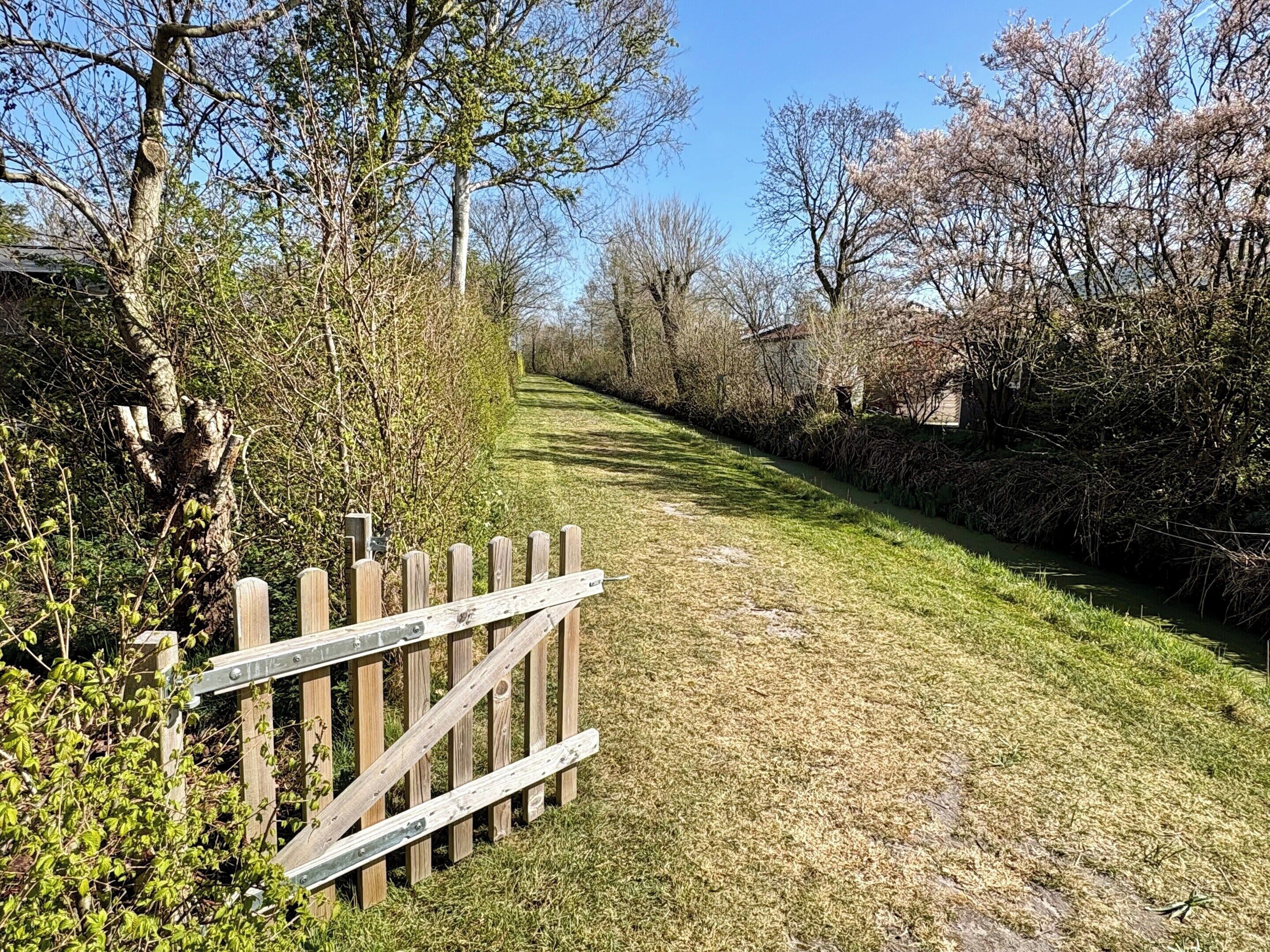 A narrow pathway with a wooden fence on one side and a grassy area on the other.