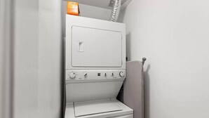 Ein kleiner, weißer Hauswirtschaftsraum mit einer Waschmaschine mit Frontlader, einem Trockner und einem kleinen Regal mit einer Kiste mit dem Aufdruck "bounty".
