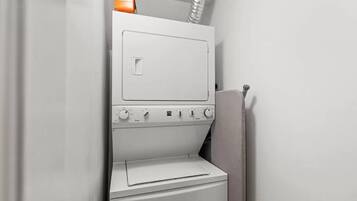 A compact, white laundry room with a built-in washer and dryer, a control panel with various settings, and a small storage area above the dryer.