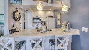 Une cuisine moderne avec des meubles blancs, un îlot central doté de tabourets de bar, un éclairage suspendu et un grand miroir mural.