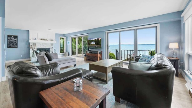 A spacious living room with a view of the sea, a fireplace, and modern furniture. - LakeHaus Vibes + Hot Tub (Traverse City)