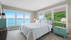 A bedroom with a large window, a bed, a nightstand, and a lamp. - LakeHaus Vibes + Hot Tub (Traverse City)