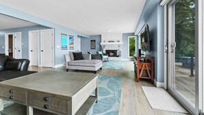 A spacious living room with a fireplace, a large TV, and a sliding glass door to a deck. - LakeHaus Vibes + Hot Tub (Traverse City)