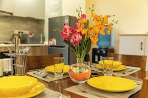 Une table  à manger dressée avec des assiettes jaunes, des verres transparents et un vase rempli de fleurs.