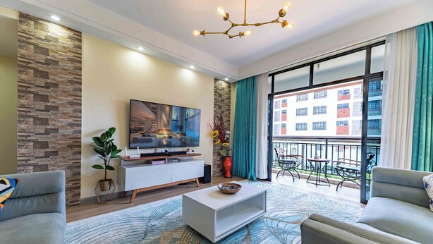 A modern living room with a flat-screen TV, a white coffee table, and a large window with a view of a building.