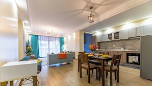 A modern kitchen with a dining area, wooden flooring, and a large window with curtains.