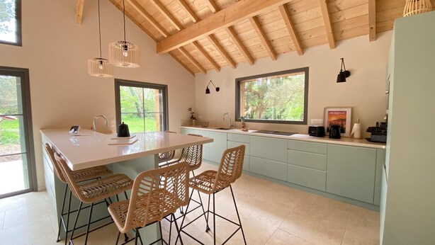 A modern kitchen with a large island, light blue cabinets, and wicker chairs. - Villa Le Charles with swimming pool ideal for large families and groups (Lit-et-Mixe)
