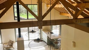 A spacious room with a high ceiling, wooden beams, a large table with chairs, and a view through a window. - Villa Le Charles with swimming pool ideal for large families and groups (Lit-et-Mixe)