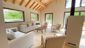 A modern living room with a sofa, chairs, and a coffee table. There are large windows and a wooden ceiling. - Villa Le Charles with swimming pool ideal for large families and groups (Lit-et-Mixe)