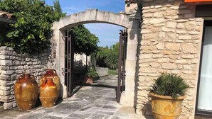 A stone archway leading to a building with a stone facade, large vases, and potted plants. - La Villa de Robion Su (Robion)
