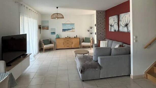 A spacious living room with a grey sofa, a TV, and a dining area with a table and chairs. - House Le Gahignon 2 (Lanton)