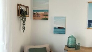 A corner room with a wooden chair, a small cabinet, and three wall-mounted artworks depicting beach scenes. - House Le Gahignon 2 (Lanton)