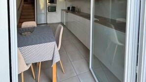 A compact kitchen with a dining area, a staircase leading to another level, and a sliding glass door. - House Le Gahignon 2 (Lanton)