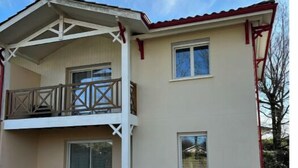 A two-story house with a balcony, a sliding glass door, and a small patio area with outdoor furniture. - House Le Gahignon 2 (Lanton)
