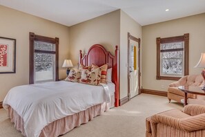 Une chambre avec un grand lit, une chaise et deux fenêtres donnant sur des arbres.