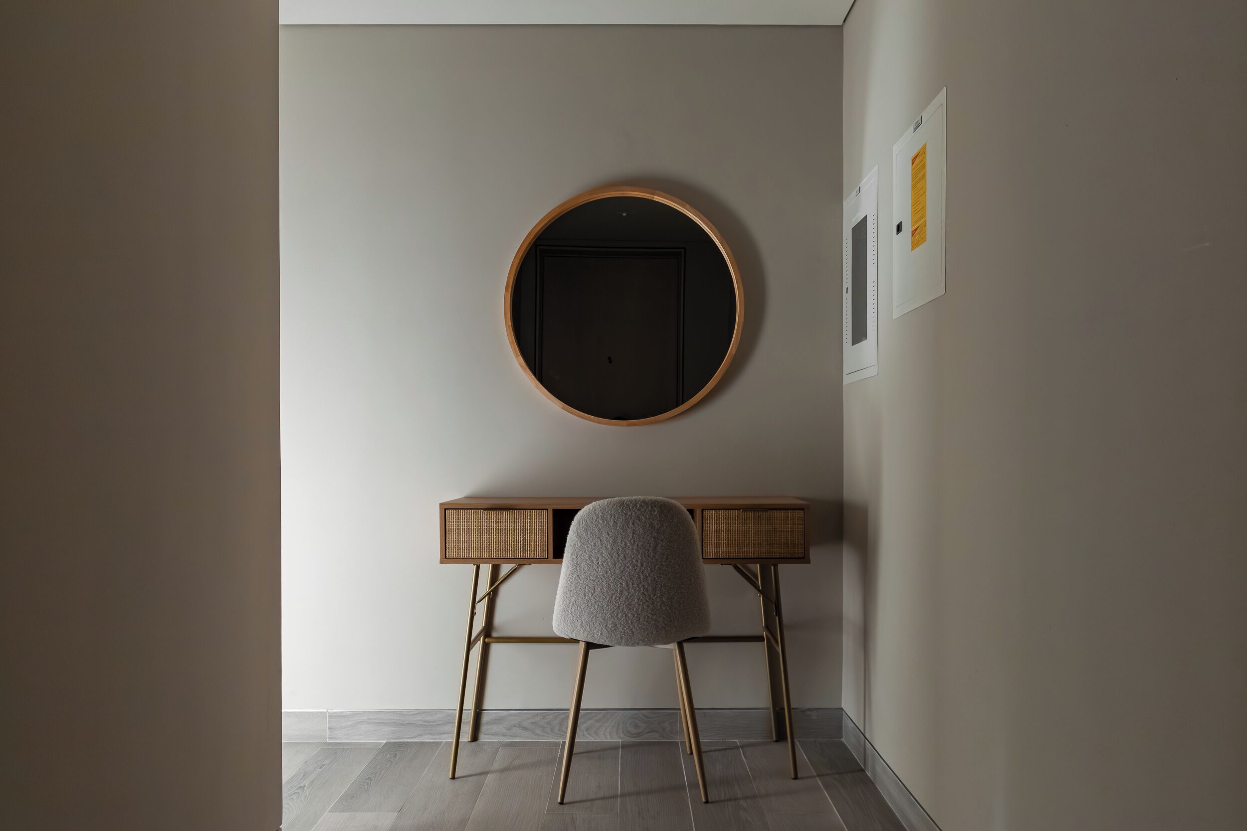 Een moderne kamer met een ronde spiegel aan de muur, een houten bureau met stoel, en een deur met een handgreep.