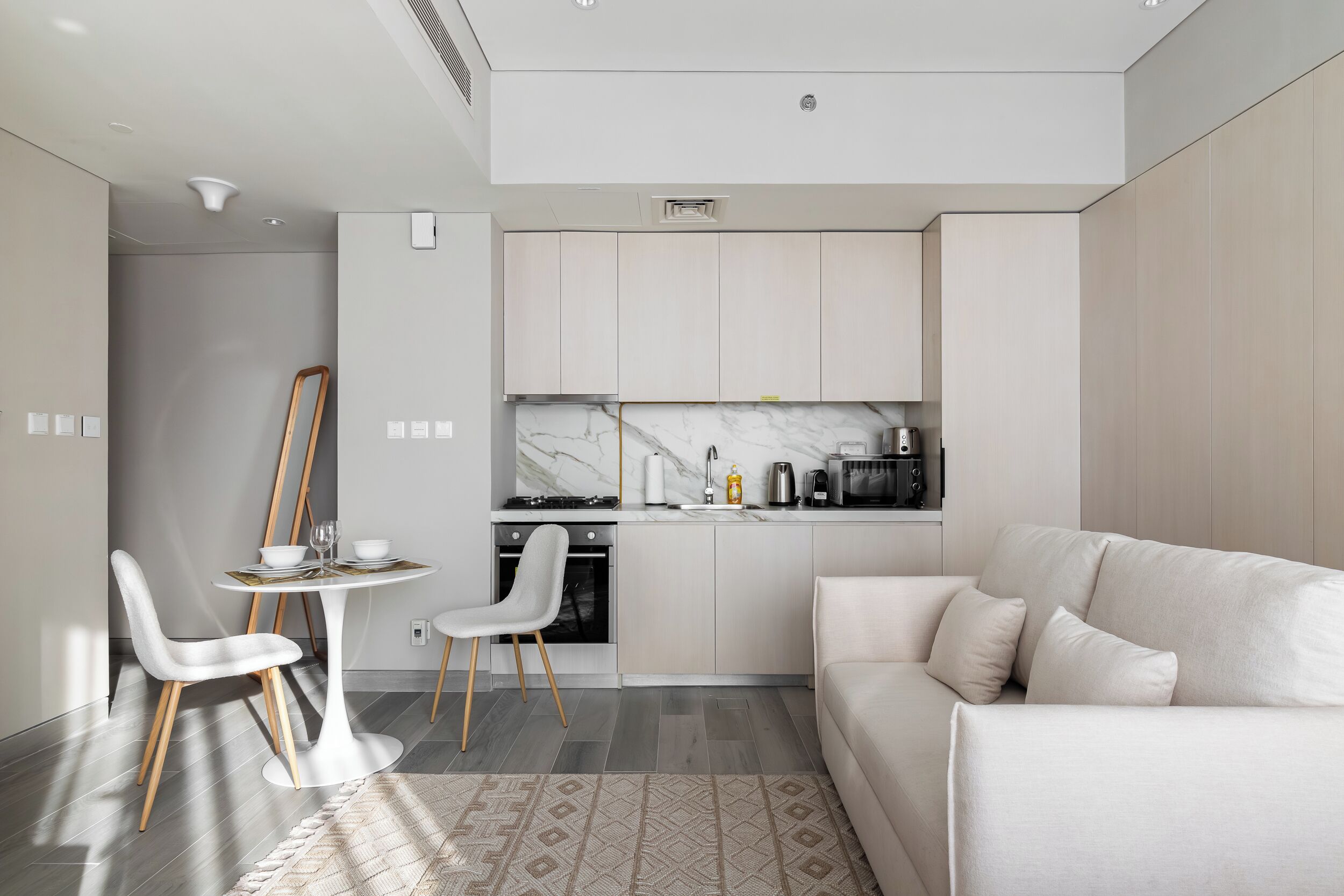 A modern kitchen with white cabinets, a marble countertop, and a dining area with a white table and chairs.