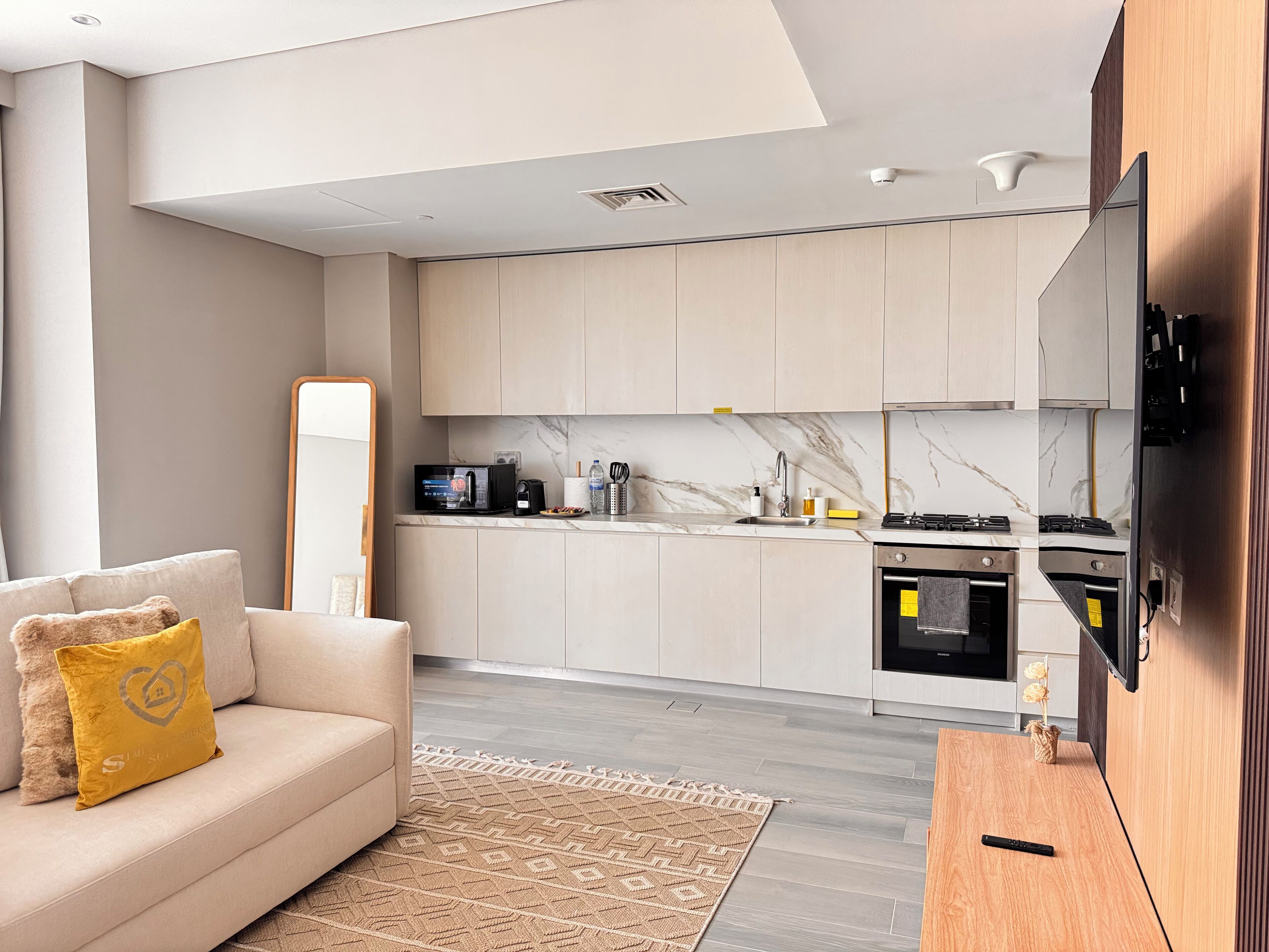 Eine moderne Küche mit integriertem Ofen, Mikrowelle und Spüle. Ein Sofa mit gelbem Kissen und ein Spiegel an der Wand sind ebenfalls vorhanden.