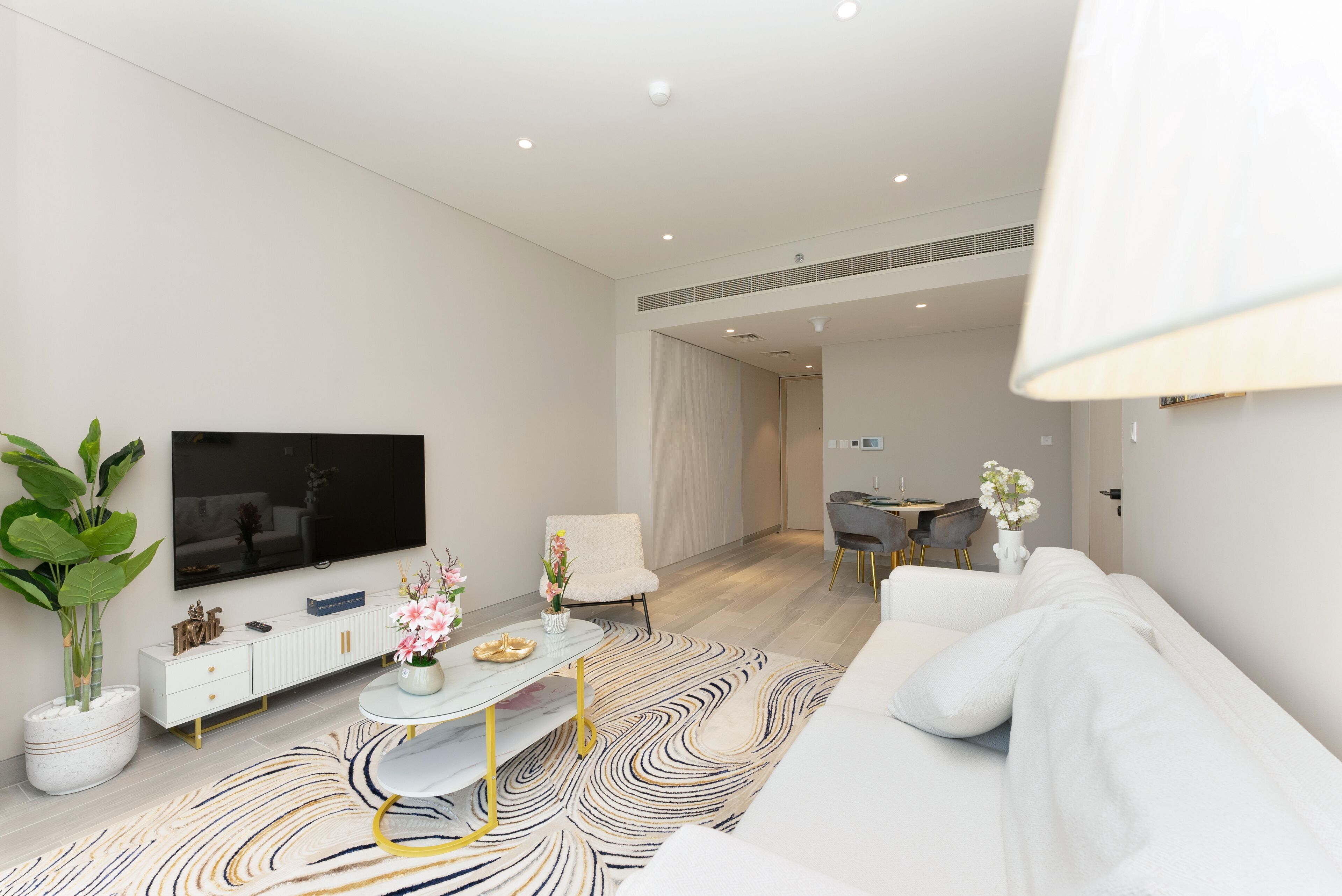 Una sala moderna con televisor de pantalla plana, sofá blanco y comedor con mesa y sillas.