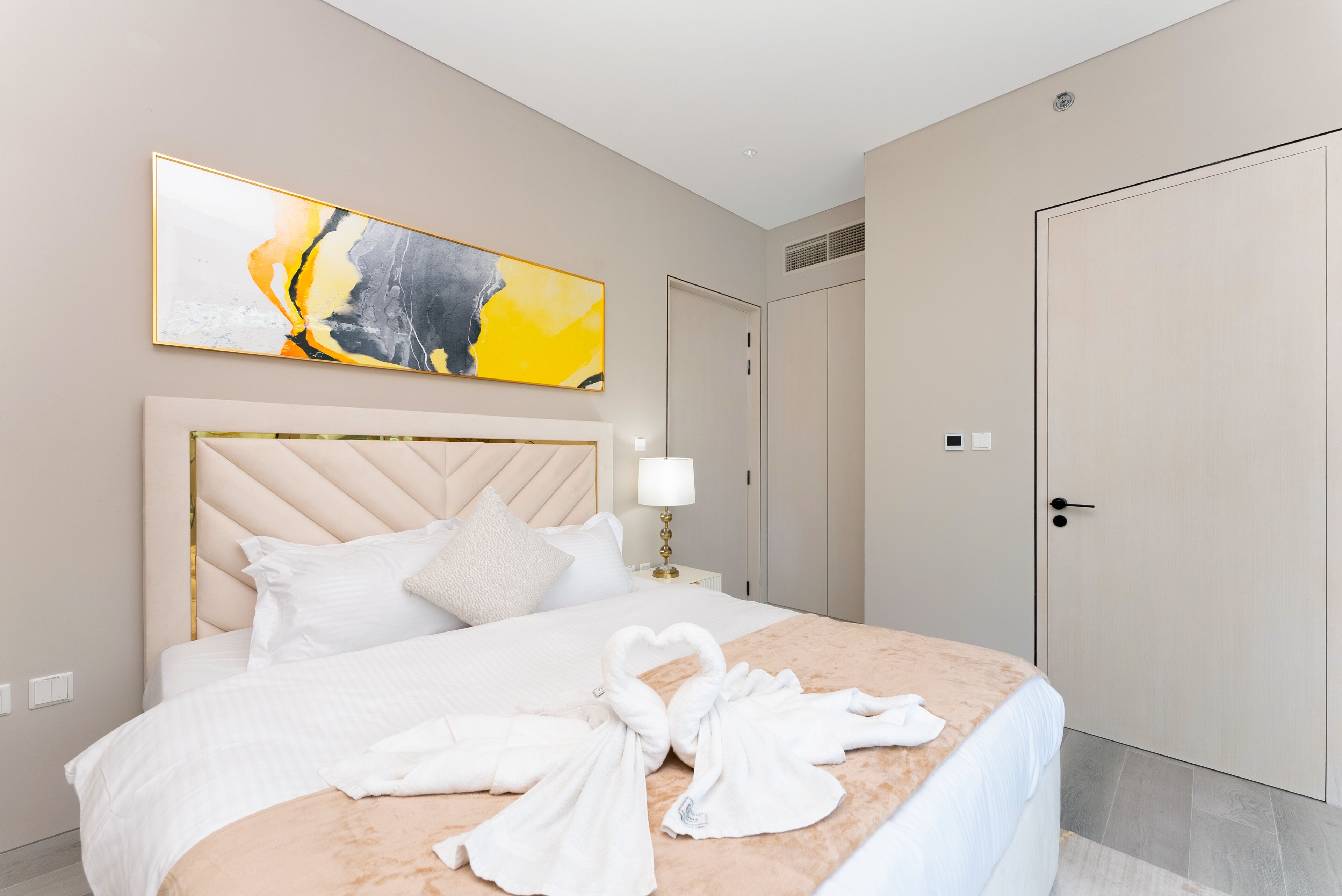 A hotel room with a large bed, a headboard, a painting, a wardrobe, and a door.