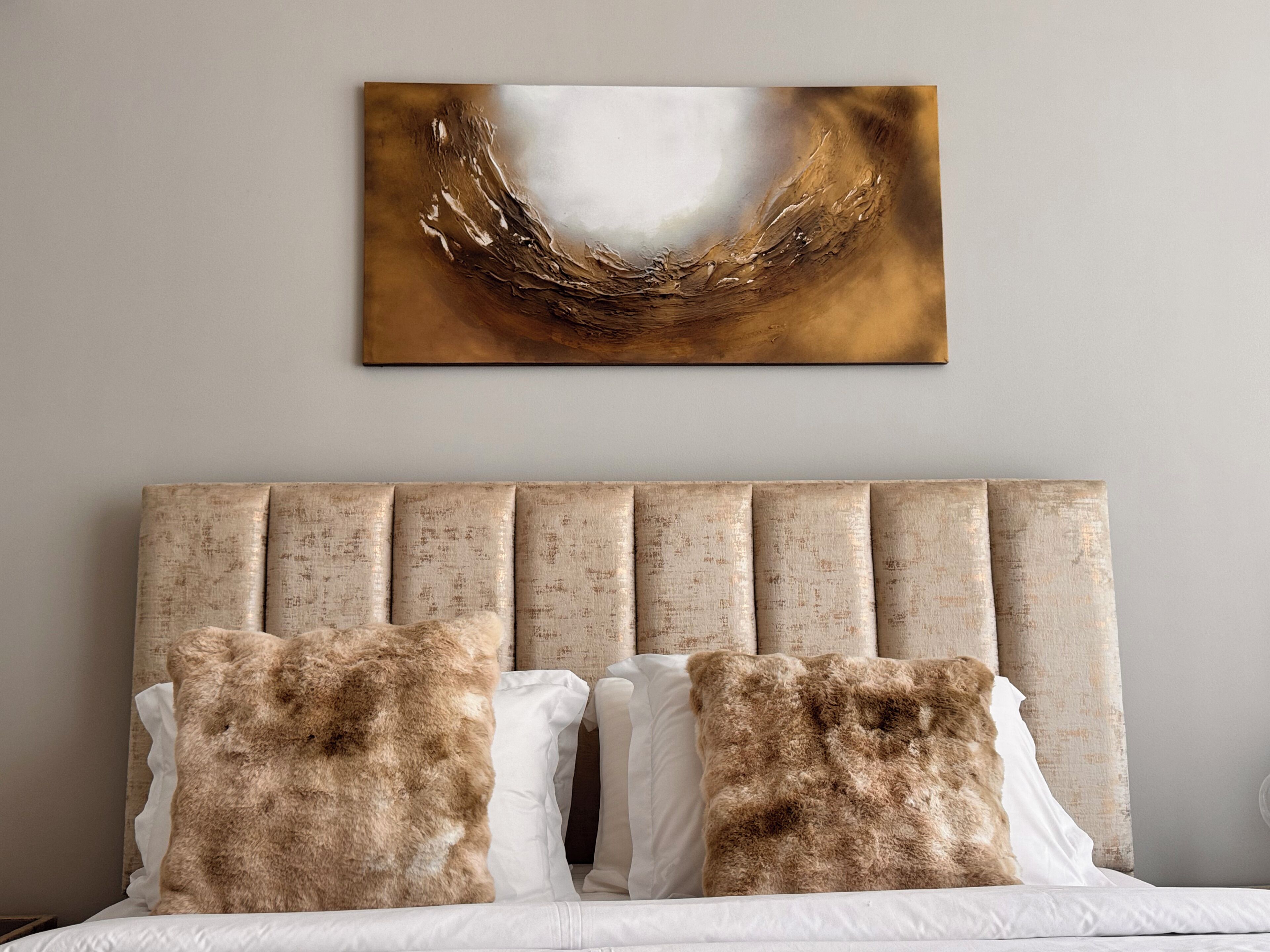 Un letto con testiera, due cuscini e un quadro astratto appeso al muro.