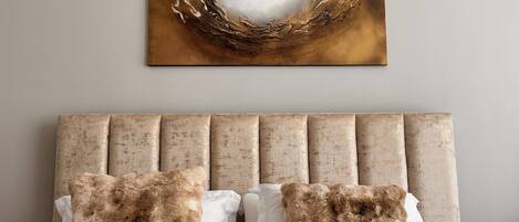 A bed with a headboard, two pillows, and a wall-mounted abstract painting.