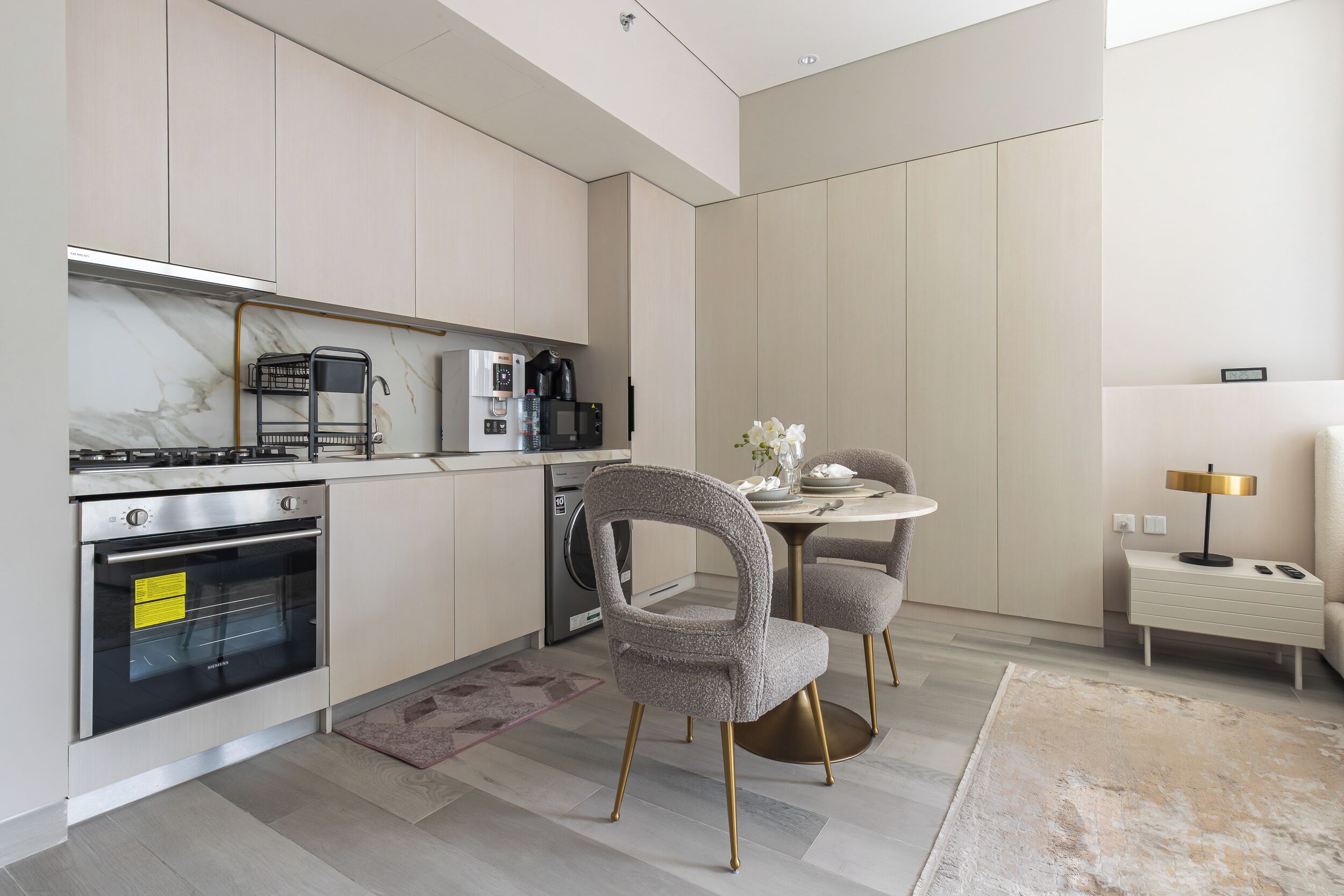 Una cucina moderna con elettrodomestici integrati, un'area pranzo con tavolo e sedie, e un comodino con una lampada.