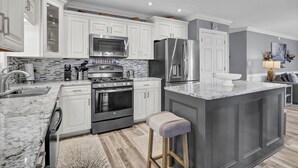 A modern kitchen with white cabinetry, a granite countertop, stainless steel appliances, and a marble island. - Waterfront Stay w/ Stunning Views, Beach Access, Outdoor Shower & Lift (North Topsail Beach)