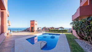 A swimming pool with a clear view of the ocean, surrounded by buildings with a uniform architectural style. - ELZE Panoramic Sea View Luxury Apartment (Calahonda)