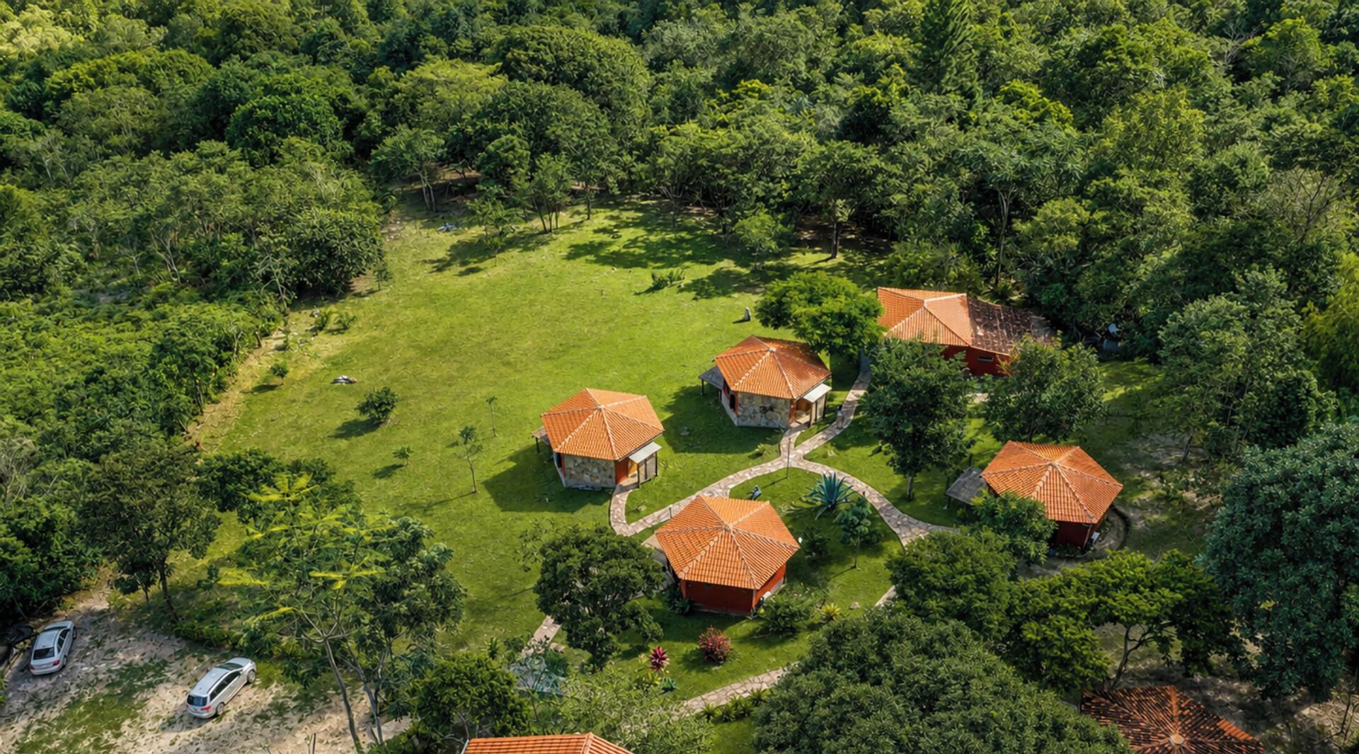 Um conjunto de pequenas casas com telhados vermelhos, cercadas por vegetação densa, com um caminho bem definido conectando-as.