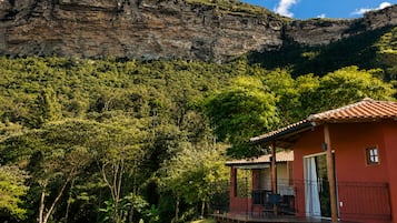Ein Haus mit roter Fassade und einem Balkon, umgeben von üppiger Vegetation und einer Bergkulisse.