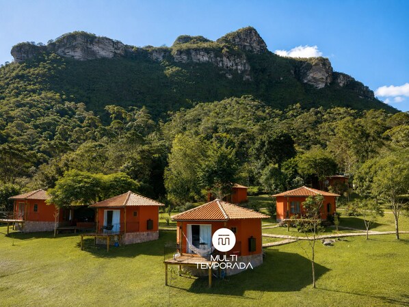 A property with multiple small buildings surrounded by lush greenery and a prominent mountain in the background.