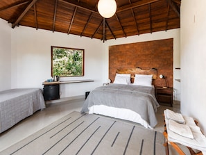 A bedroom with two beds, a brick accent wall, a window with a view, and a ceiling fan.