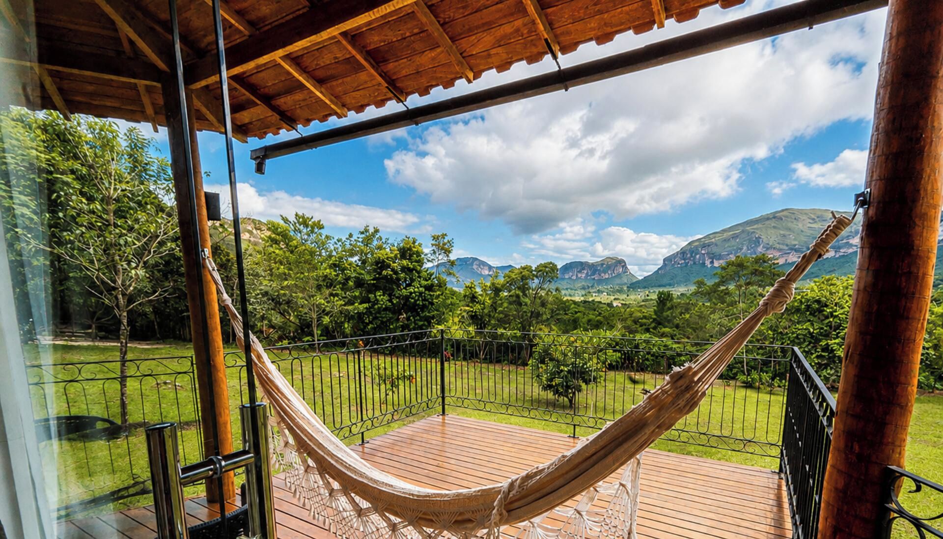 Una hamaca en una terraza de madera con vistas a montañas y vegetación.