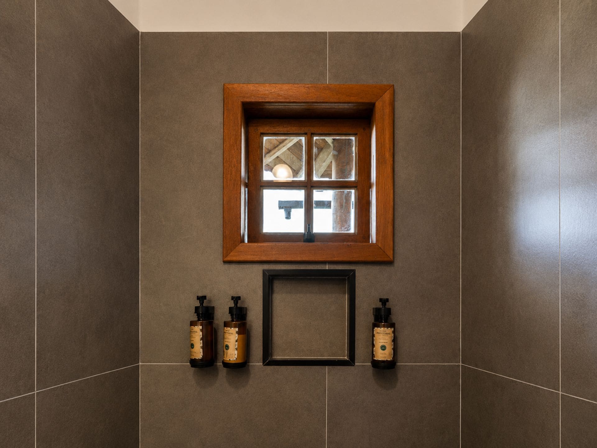 Un baño con ventana de madera, paredes enlosadas y dos botellas de loción en el suelo.