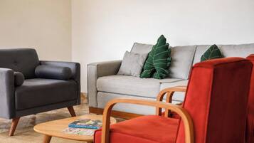 A living room with a grey sofa, a black armchair, and a wooden coffee table with magazines.