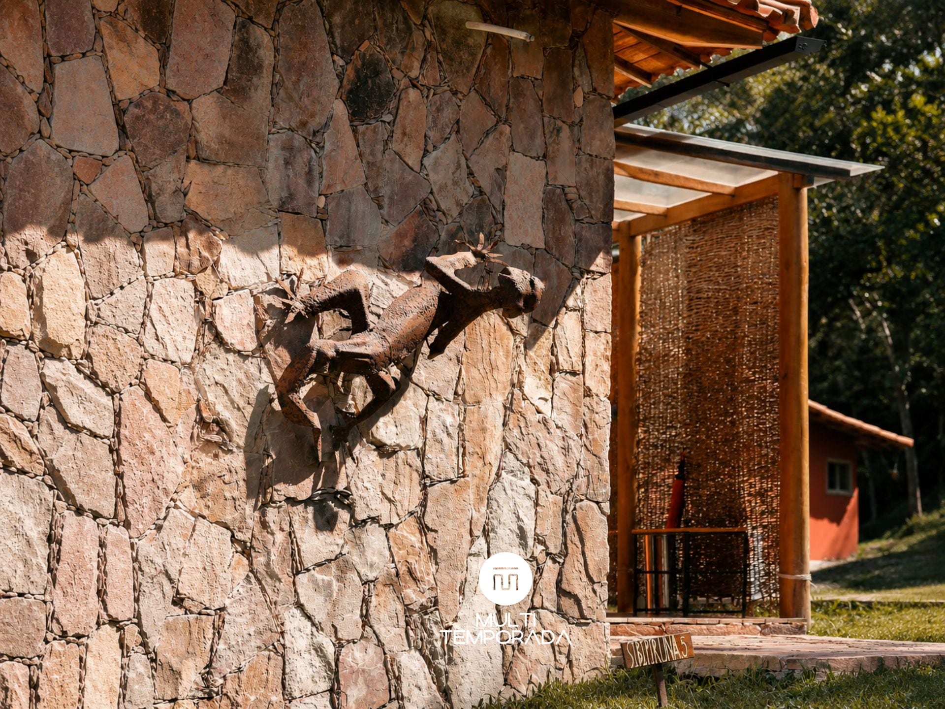 Un muro de piedra con una escultura de cabeza de animal montada, una puerta de madera y un letrero que dice 'MULTI TEMPORADA'.