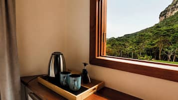A wooden tray with a kettle and two mugs on a windowsill, overlooking a forested hillside.