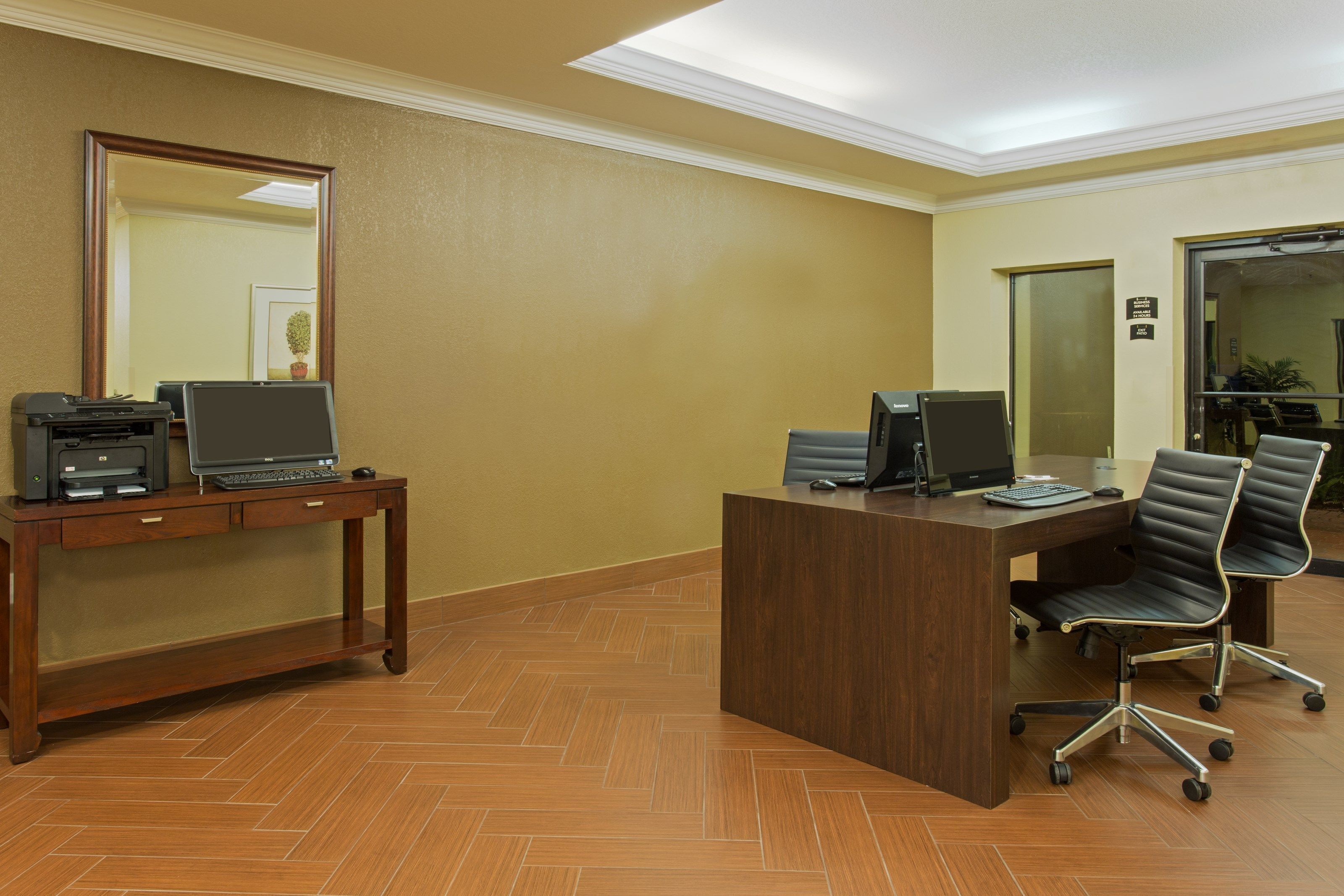 A reception desk with a computer, a printer, and a telephone. There is a mirror on the wall and a door to the right.