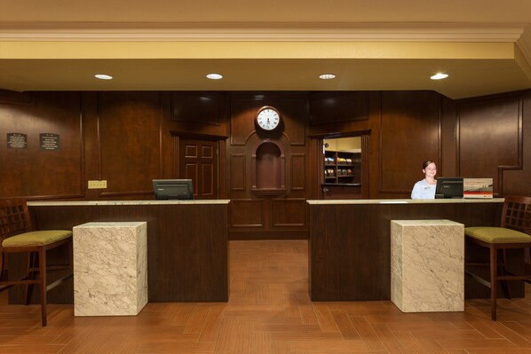 Classic reception area with a central clock, marble-topped counters, and dark wood paneling.