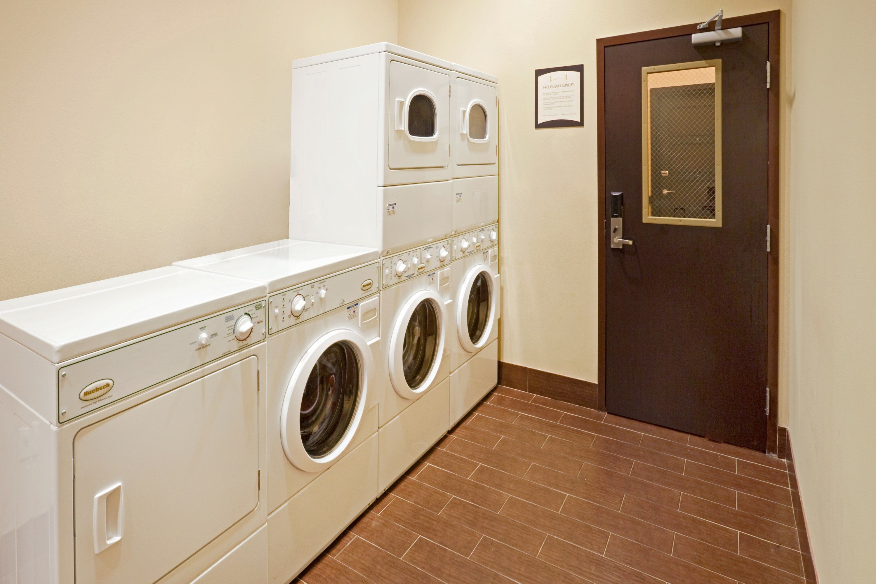 A laundry room with a large washer and dryer unit, a door with a security screen, and a tiled floor.