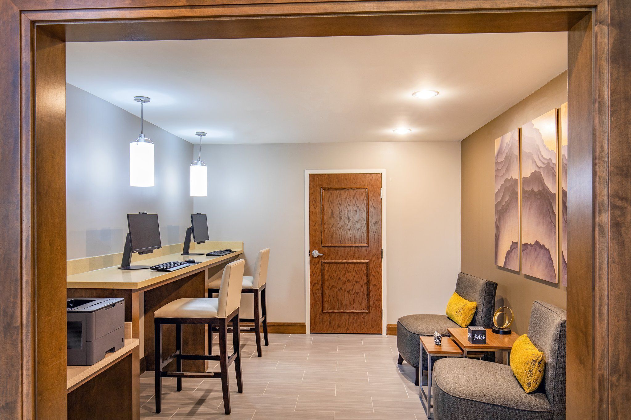 A hotel room with a desk, two chairs, a sofa, a door, and a wall with artwork.
