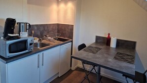 A compact kitchen with a microwave, coffee maker, and sink. There is a small table with a chair and a bottle of water. - Glaz - T1bis in the heart of Pllemeur (Ploemeur)