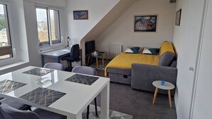 A compact room with a bed, a sofa, a dining table, and a small TV. - Glaz - T1bis in the heart of Pllemeur (Ploemeur)